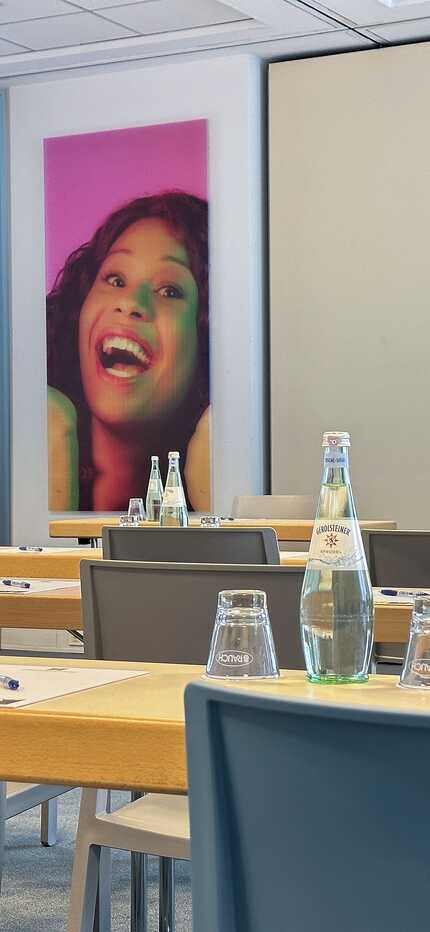A conference room is set with chairs and tables, featuring vibrant portraits on the walls and bottled water on the tables.