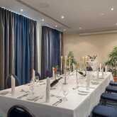 A beautifully arranged banquet table is set with elegant tableware, candles, and surrounded by lush green plants.