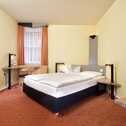 A cozy double room features a comfortable bed, a desk with a chair, and modern decor in warm tones.