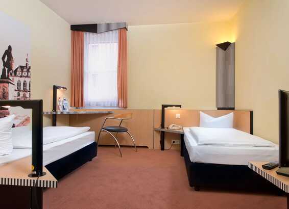 A cozy twin bed room features simple decor, a desk with a chair, and a painting on the wall.