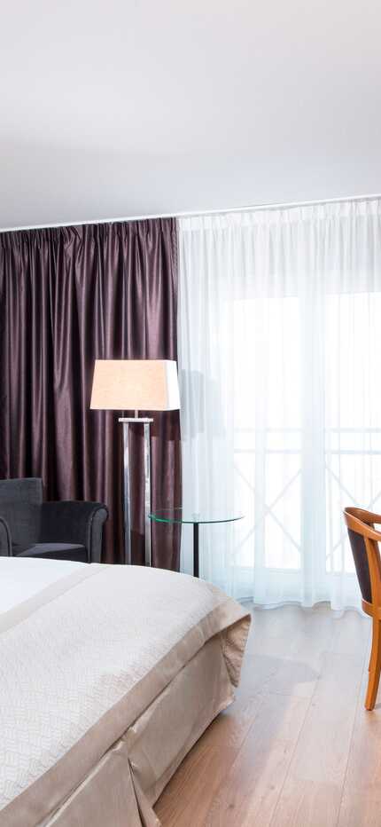 A modern double room features a cozy bed, a work desk, and elegant decor with soft lighting and dark curtains.