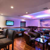 Eine moderne Hotelbar mit gemütlichen Sitzgelegenheiten und einem Fernseher, beleuchtet in sanften Farben.