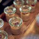 Small glass jars filled with oatmeal topped with fruit are neatly arranged on a wooden tray for breakfast.