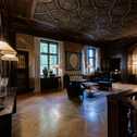 Ein elegantes Zimmer mit kunstvoller Decke, stilvollen Möbeln und großen Fenstern, die den Raum erhellen.