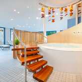 A luxurious indoor jacuzzi with wooden steps and modern decor is set in a serene spa-like environment.