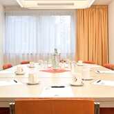 Ein heller Konferenz- oder Tagungsraum im Best Western Hotel Achim Bremen, vorbereitet für ein Meeting. Ein großer, sechseckiger Tisch steht im Mittelpunkt, umgeben von orangefarbenen Stühlen. Jeder Platz ist mit Tassen, Untertassen, einem Notizblock und