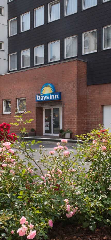 Colorful flowers bloom in front of a Days Inn hotel exterior on a quiet urban street.