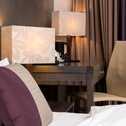 Ein elegantes Deluxe-Zimmer mit modernem Schreibtisch, stilvollen Lampen und gemütlichem Bett mit lila Kissen.
