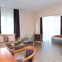 A modern apartment living room with a cozy sofa, TV, and natural light streaming through large windows.
