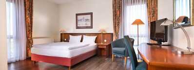 A spacious double room features a neatly made bed, wooden furniture, and a desk with a TV, creating a cozy atmosphere.