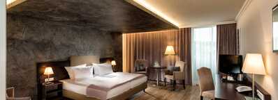 A modern deluxe hotel room features a large bed, ambient lighting, and elegant furnishings for a luxurious stay.