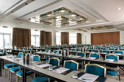 A spacious meeting room with neatly arranged blue chairs and tables, set up for a conference with notepads and water bottles.