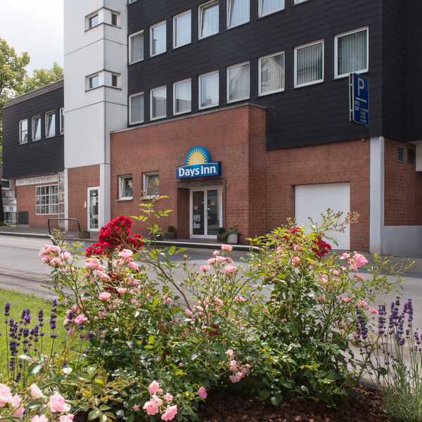 Colorful flowers bloom in front of a Days Inn hotel exterior on a quiet urban street.