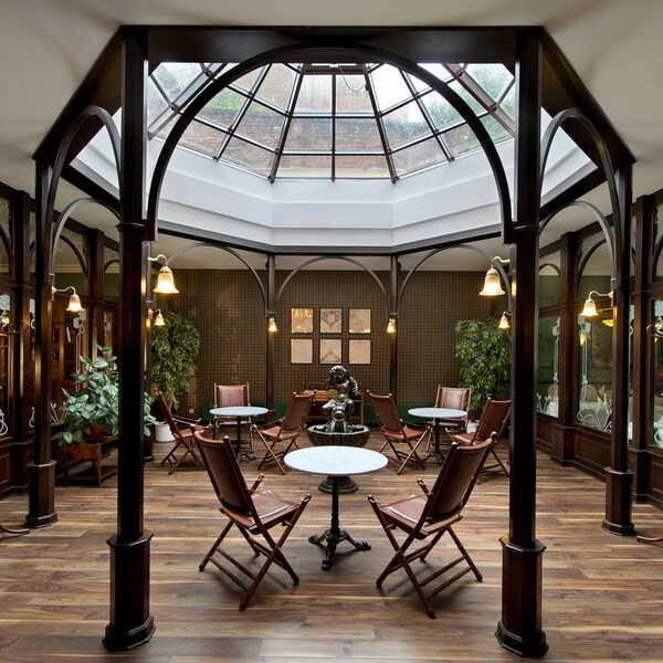 A spacious atrium lobby features a glass ceiling, elegant wooden furnishings, and lush plants, creating a welcoming ambiance.