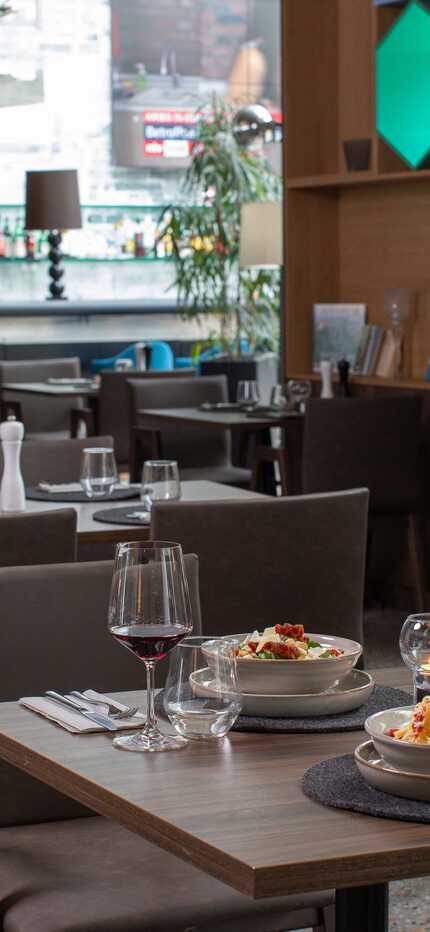 Ein modernes Restaurant mit gedeckten Tischen, servierten Pasta-Gerichten und einer Bar im Hintergrund.