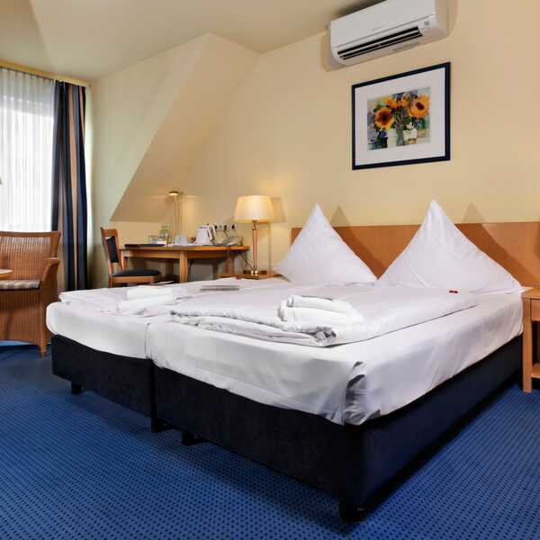 A cozy double room features a neatly made bed, wicker chairs, and a table with wine, creating a welcoming atmosphere.