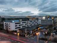 Das Bild zeigt das Äußere eines Wyndham-Hotels bei Dämmerung, umgeben von Straßen und beleuchteten Gebäuden.