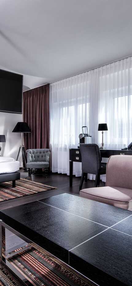 A modern suite features a cozy seating area, stylish decor, and a large bed, creating a comfortable and elegant atmosphere.