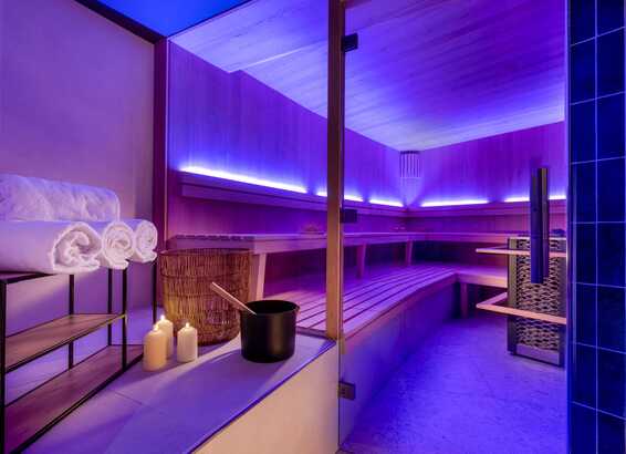Eine moderne Sauna mit blauer Beleuchtung, Holzbänken und bereitliegenden Handtüchern lädt zum Entspannen ein.