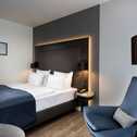 A modern executive room features a stylish bed, blue chair, and a sleek lamp, creating a cozy atmosphere.