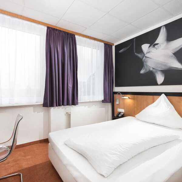 Ein modernes Einzelzimmer mit einem gemütlichen Bett, einem Schreibtisch und einem großen Blumenbild an der Wand.