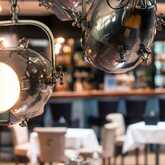Elegant industrial-style lights illuminate a chic hotel bar with tables and chairs in the background.