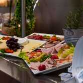 A breakfast buffet features a variety of cold cuts, cheeses, and fresh grapes on a platter.