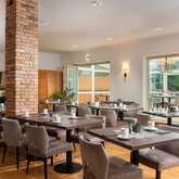 A modern restaurant interior features neatly arranged tables with chairs, a brick pillar, and large windows for natural light.