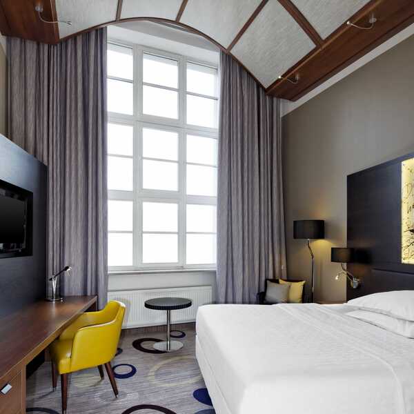 Ein modernes Hotelzimmer mit großem Fenster, gelbem Stuhl und elegantem Design lädt zum Entspannen ein.