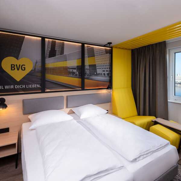 Ein modernes Berliner Hotelzimmer mit gelbem Sessel und Blick auf den Fluss durch das Fenster.