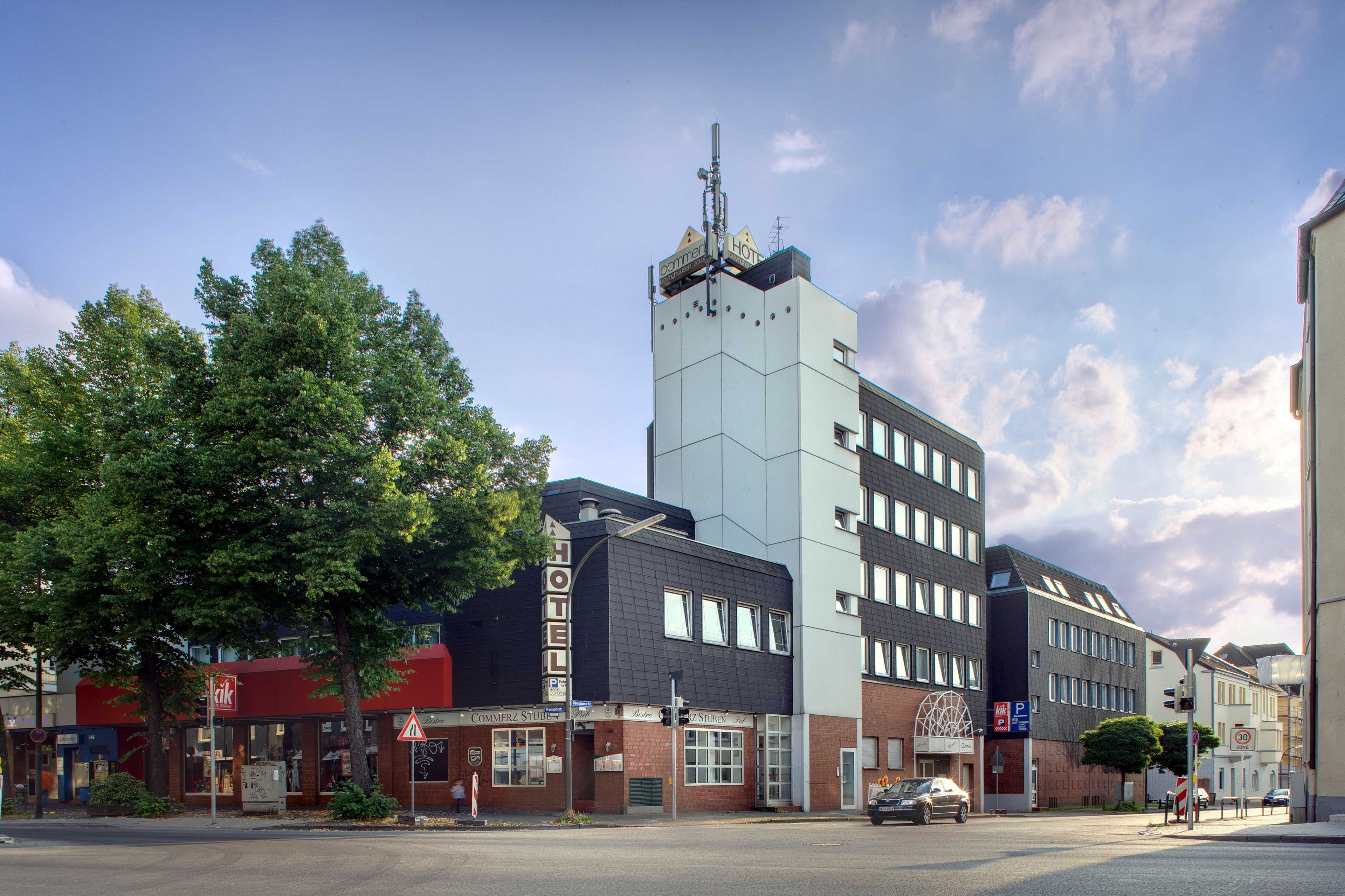 The exterior view shows a modern hotel building with a prominent sign and nearby trees under a partly cloudy sky.