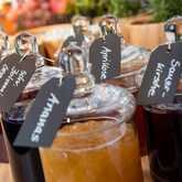 Assorted fruit jams in glass jars are neatly arranged on a breakfast table, each labeled with black tags.