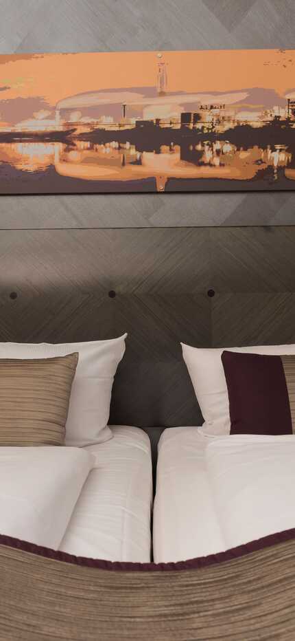 A deluxe hotel room features two neatly made beds, warm lighting, and a cityscape painting above the headboard.
