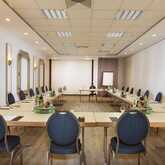 A U-shaped meeting room setup with blue chairs and tables equipped with notepads and drinks, ready for a conference.