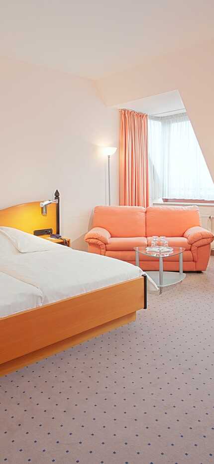 Ein gemütliches Doppelzimmer mit zwei Betten, einer rosa Couch und einem Schreibtisch mit Fernseher in einem hellen Raum.
