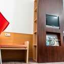 A modern room features a red chair, wall-mounted TV, and magazines on a wooden shelf, creating a cozy atmosphere.