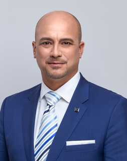 A confident man in a blue suit and striped tie poses against a plain background.