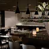 A stylish restaurant interior features elegant tables, soft lighting, and a large orchid arrangement on a sleek countertop.