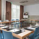 A conference room is set up with a U-shaped table arrangement, complete with notepads, pens, and glasses for a meeting.