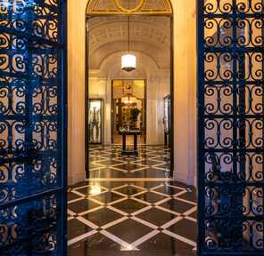 An ornate entrance gate opens to a luxurious hallway with checkered floors and elegant lighting.
