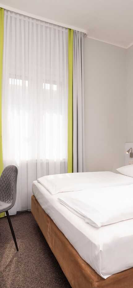 Ein modernes, helles Hotelzimmer mit Doppelbett, Flachbildfernseher und farbenfrohem Wandbild lädt zum Entspannen ein.