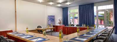 A spacious meeting room with a U-shaped table setup, featuring blue notepads and bottled water for attendees.