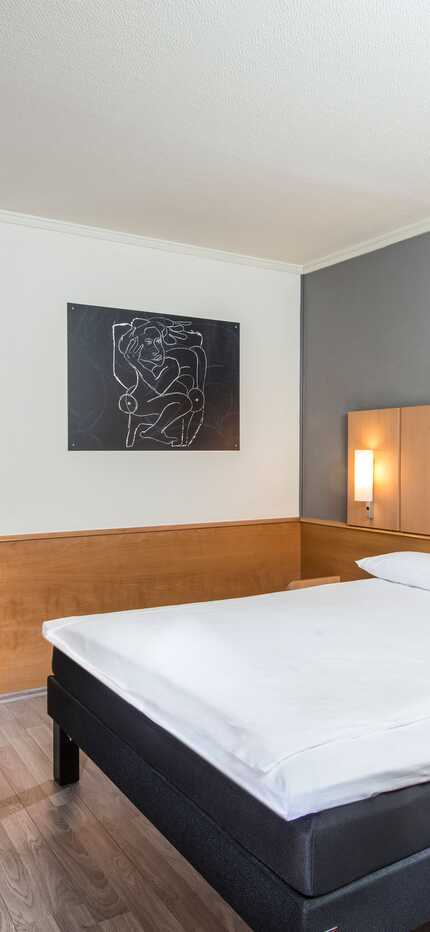 Ein modernes Einzelzimmer mit einem gemütlichen Bett, Schreibtisch und stilvoller Kunst an der Wand.
