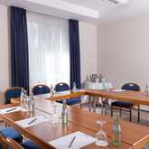 A well-lit meeting room with arranged tables, chairs, notepads, and bottled water awaits attendees.