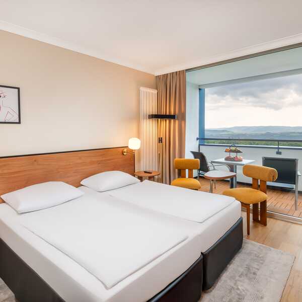 Ein modernes Hotelzimmer mit Doppelbett und Balkon bietet eine atemberaubende Aussicht auf die Landschaft.