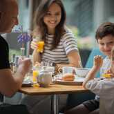 A family enjoys breakfast together at a table, with orange juice and pastries creating a joyful morning atmosphere.