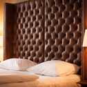 A cozy bed with a tufted leather headboard is flanked by two elegant lamps, creating a warm and inviting atmosphere.