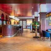 A stylish bar features a curved wooden counter, elegant lighting, and cozy seating, creating an inviting atmosphere.