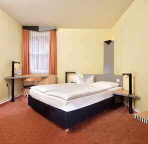 A cozy double room features a comfortable bed, a desk with a chair, and modern decor in warm tones.