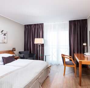 A modern double room features a cozy bed, a work desk, and elegant decor with soft lighting and dark curtains.